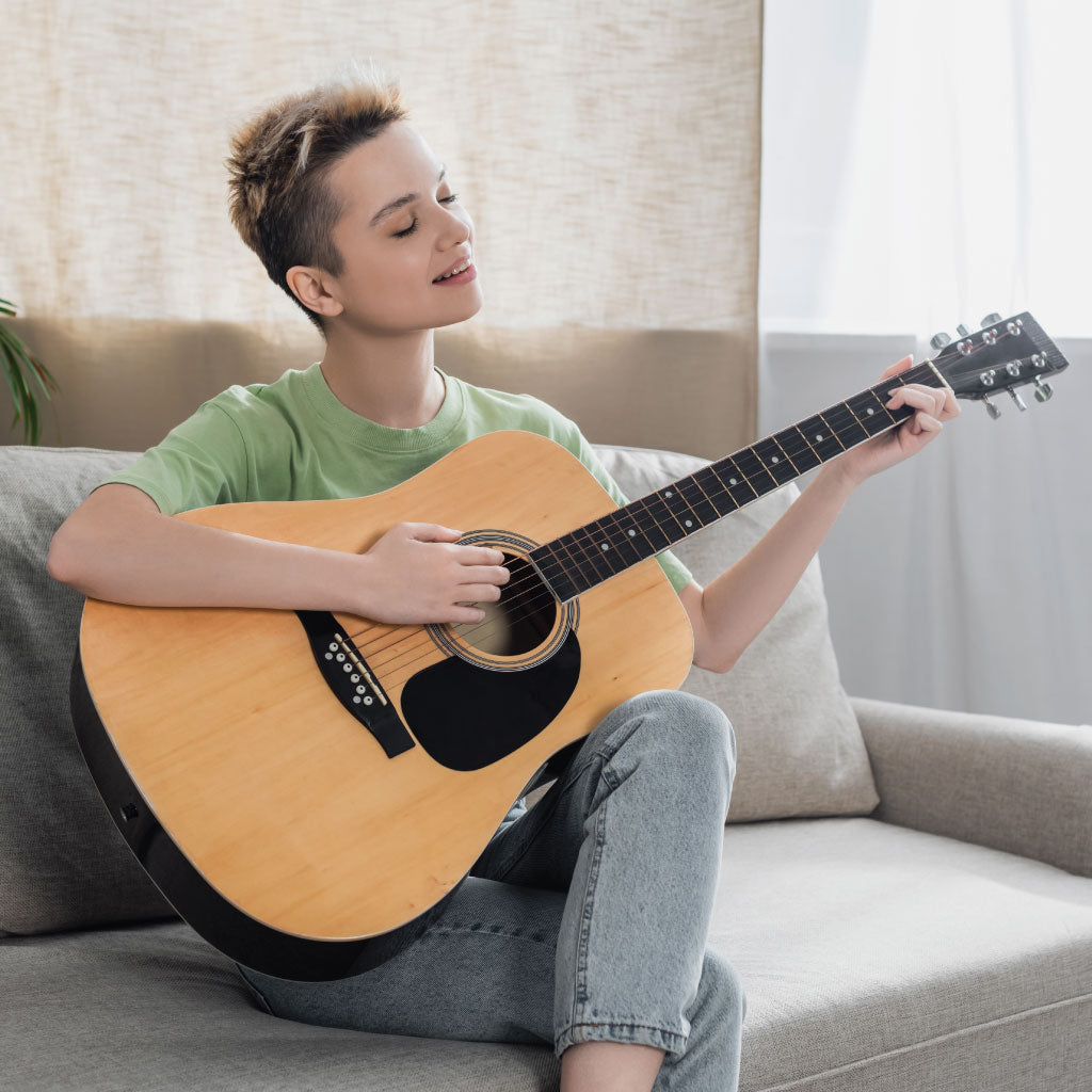 Pangender person sitting on the sofa, playing an acoustic guitar