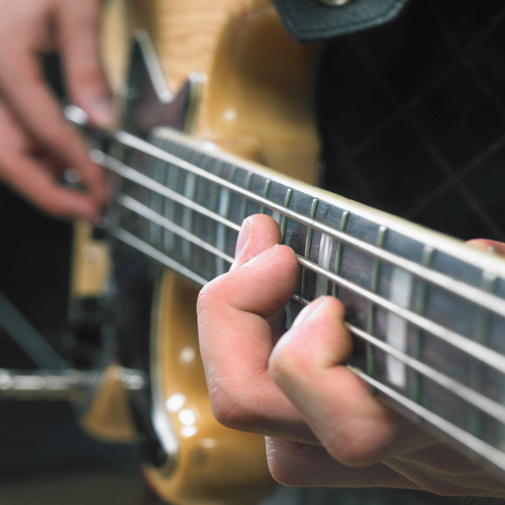 Cropped image of someone playing a bass guitar. All that is visible is the bass guitar body, part of the neck, and the hands playing