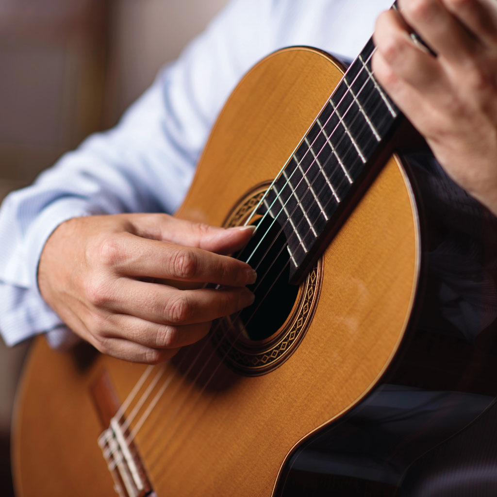 close-up of a man playing the classical guitar. Only the guitar body and hands are visible