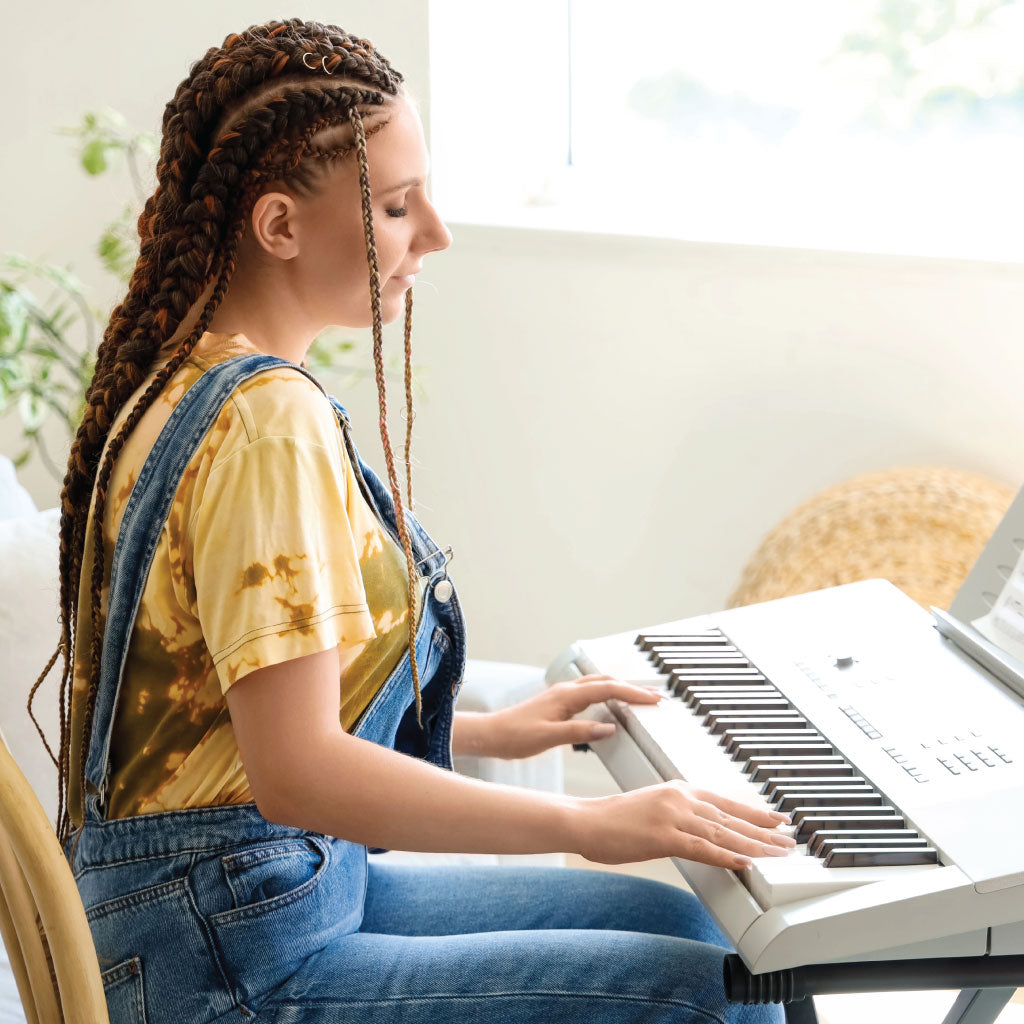 Woman with dreadlocks and wearing dungarees, sitting and playing an electronic keyboard